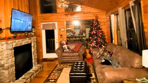 A cozy log cabin interior with a fireplace, a television, a Christmas tree, and a leather sofa. - 2 Min to Dollywood!  5 min To Pigeon Forge! Come check us out!!! (Sevierville)
