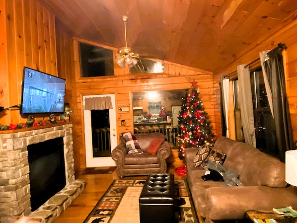 L’intérieur d’un chalet confortable en bois, avec une cheminée, un téléviseur, un sapin de Noël et un canapé en cuir.