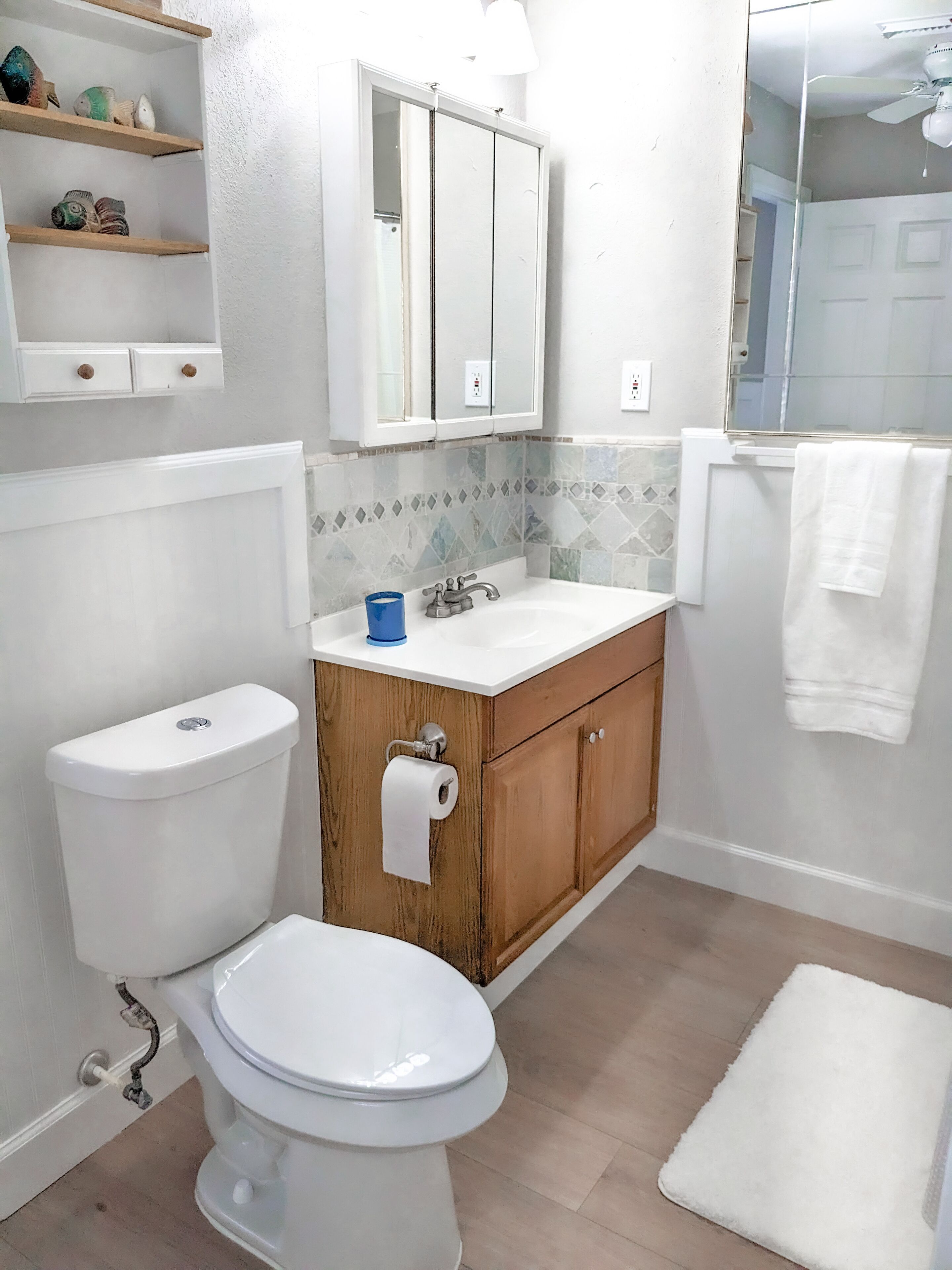 A bathroom with a toilet, sink, wooden vanity, and a mirror.