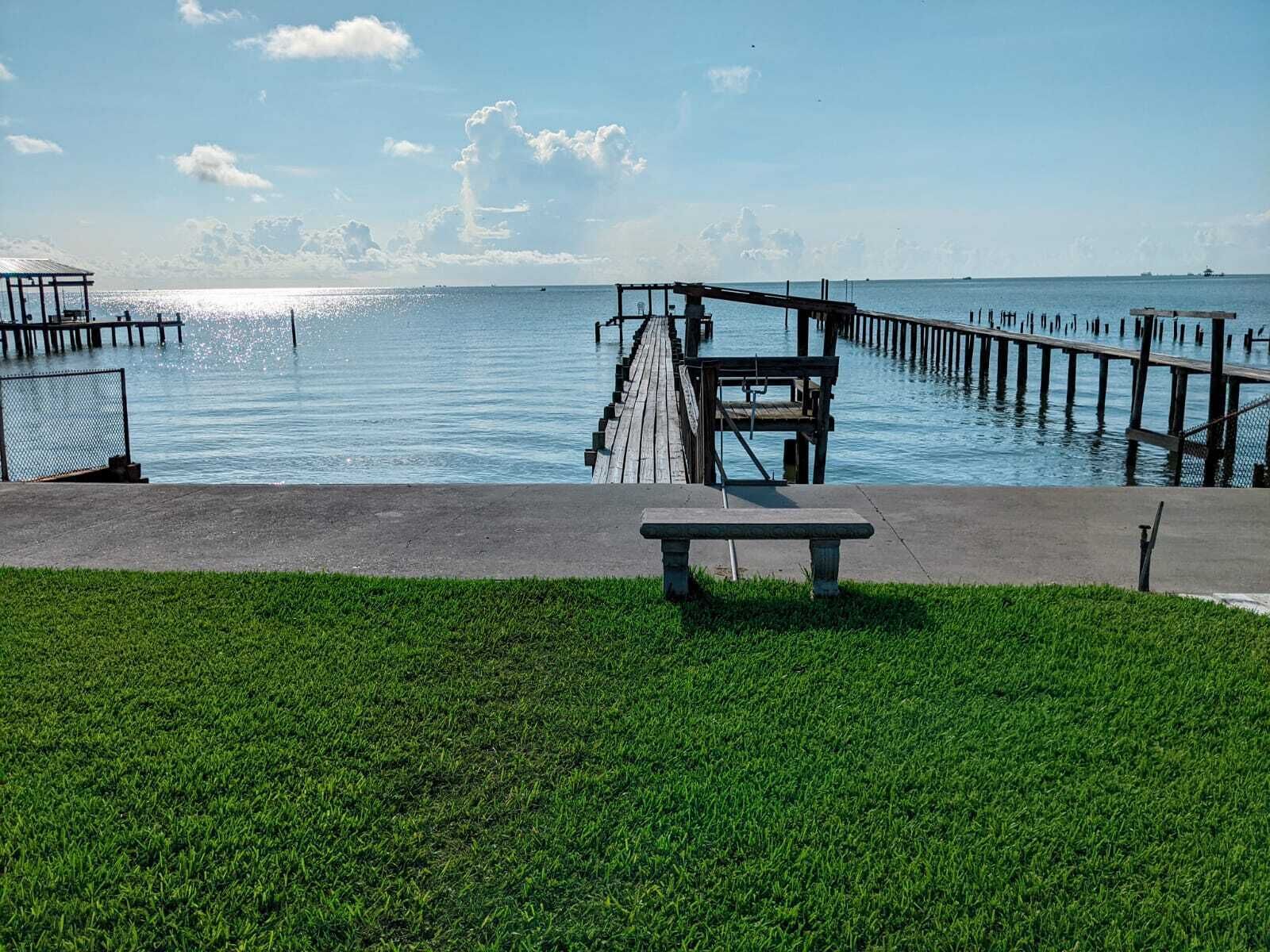 A pier extending into calm water with a grassy area in the foreground and a bench.