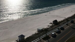 A beach with a road running parallel to it, a lifeguard tower, and a clear sky.