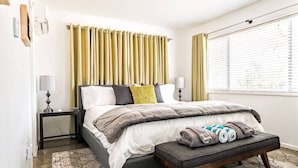 A bedroom with a bed, bedside tables, a bench, and a window with curtains. - Joshua Tree Getaway Private Desert Views (Yucca Valley)