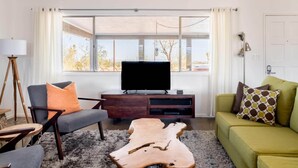 A modern living room with a grey sofa, a green sofa, a wooden coffee table, and a television on a wooden cabinet. - Joshua Tree Getaway Private Desert Views (Yucca Valley)