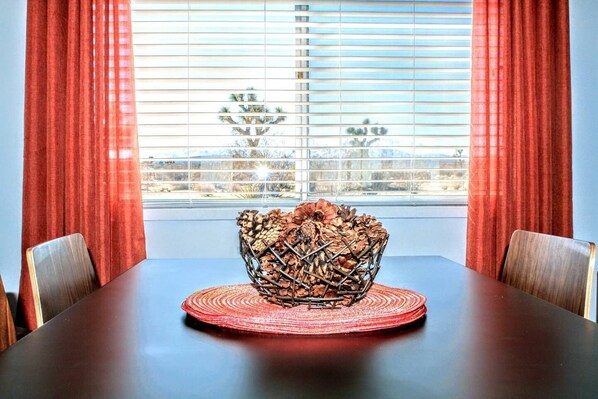 A dining table with a woven centerpiece, red curtains, and a window with blinds. - Joshua Tree Getaway Private Desert Views (Yucca Valley)
