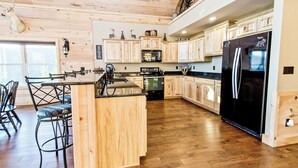 Una cocina amplia con armarios de madera, un refrigerador negro y un comedor con sillas.