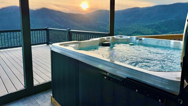 Un jacuzzi en una terraza de madera con vista a la montaña al atardecer.