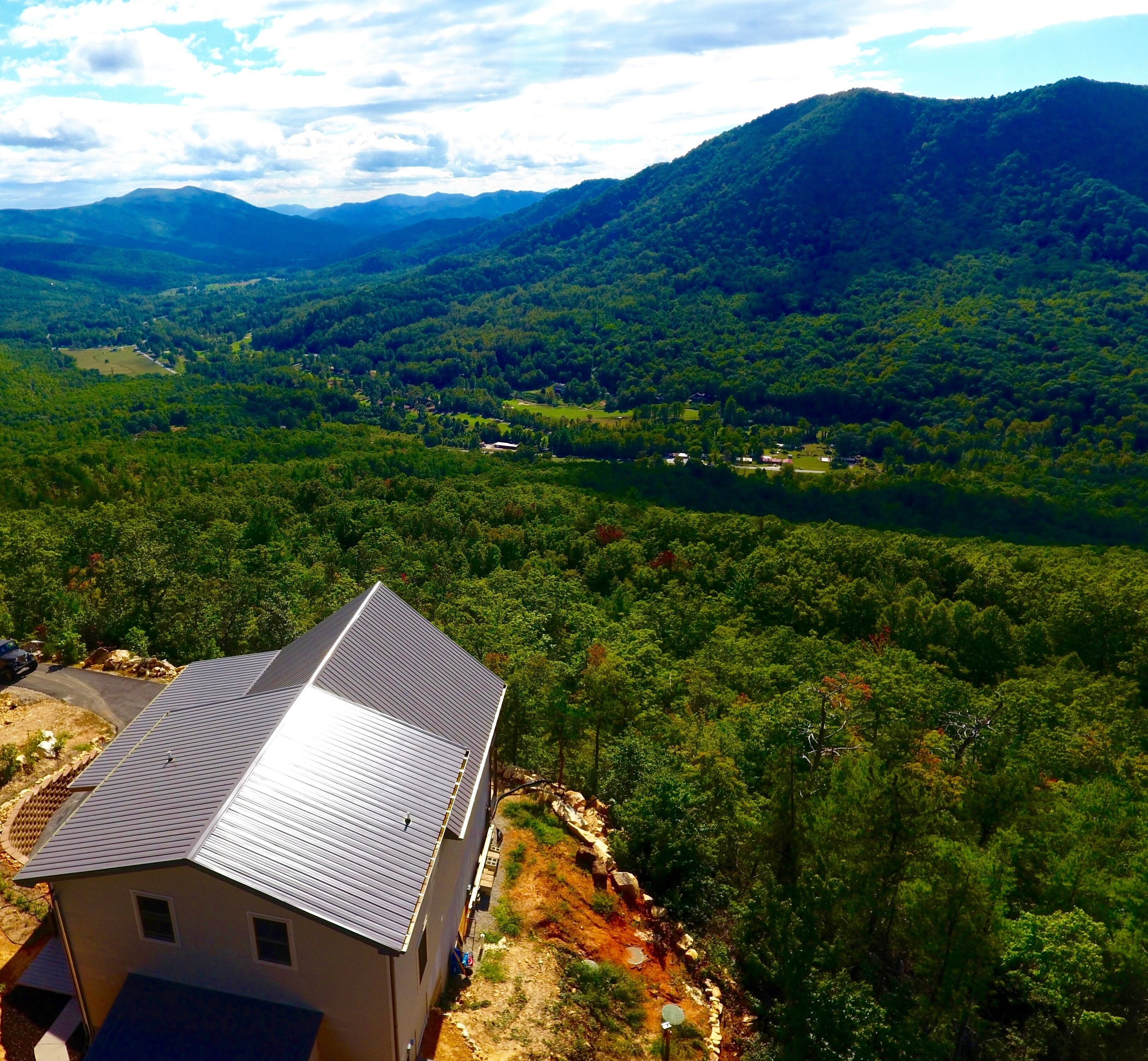 Une maison avec un toit en métal, entourée d’une forêt dense et de montagnes.