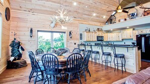 Interior de una cabaña de madera con comedor, cocina y barra.