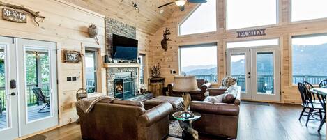 A spacious living room with a fireplace, leather sofas, and a dining area with a view of the mountains.