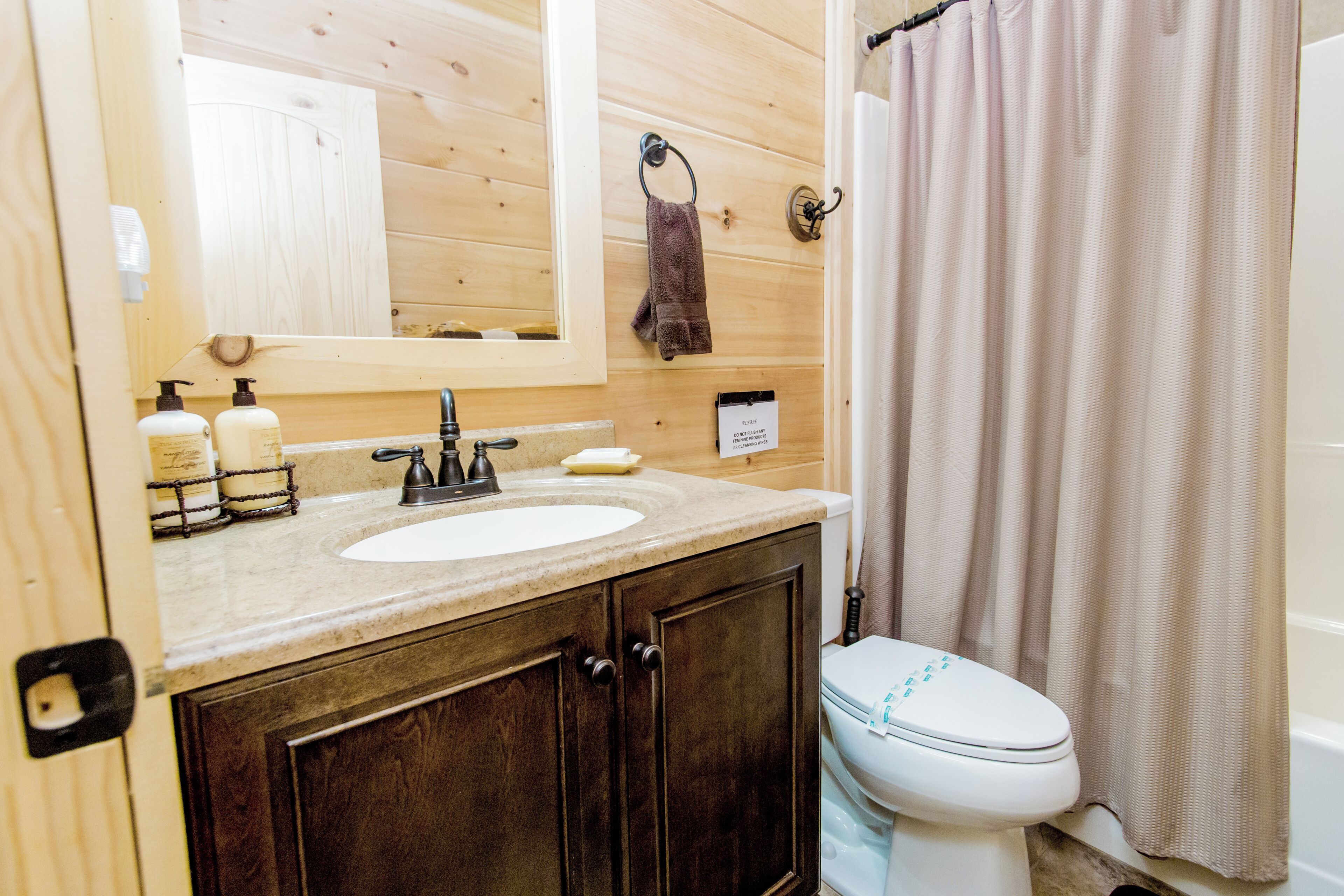A bathroom with a wooden vanity, a sink, a mirror, a towel ring, and a toilet.