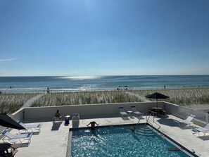 A pool area with lounge chairs and a view of the ocean.