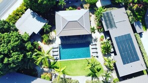 An aerial view of a residential area with a swimming pool, solar panels, and lush greenery. - Villa 6 (Kihei)