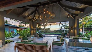 A covered outdoor lounge area with seating, a pool, and a view of palm trees and the ocean. - Villa 6 (Kihei)