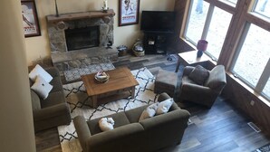 Una sala de estar acogedora con chimenea de piedra, televisión y un amplio ventanal con vistas al exterior.