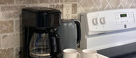 Uma cozinha com uma cafeteira Toastmaster preta, duas canecas brancas, uma chaleira elétrica cinza e um fogão branco.