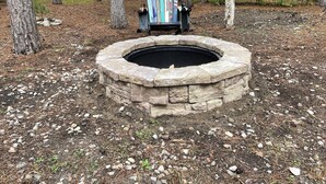 Un hogar de piedra rodeado por un área boscosa con árboles y una silla de metal con esquíes apoyados en ella.