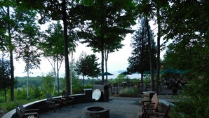 An outdoor seating area with a circular fire pit, wooden chairs, and tables.