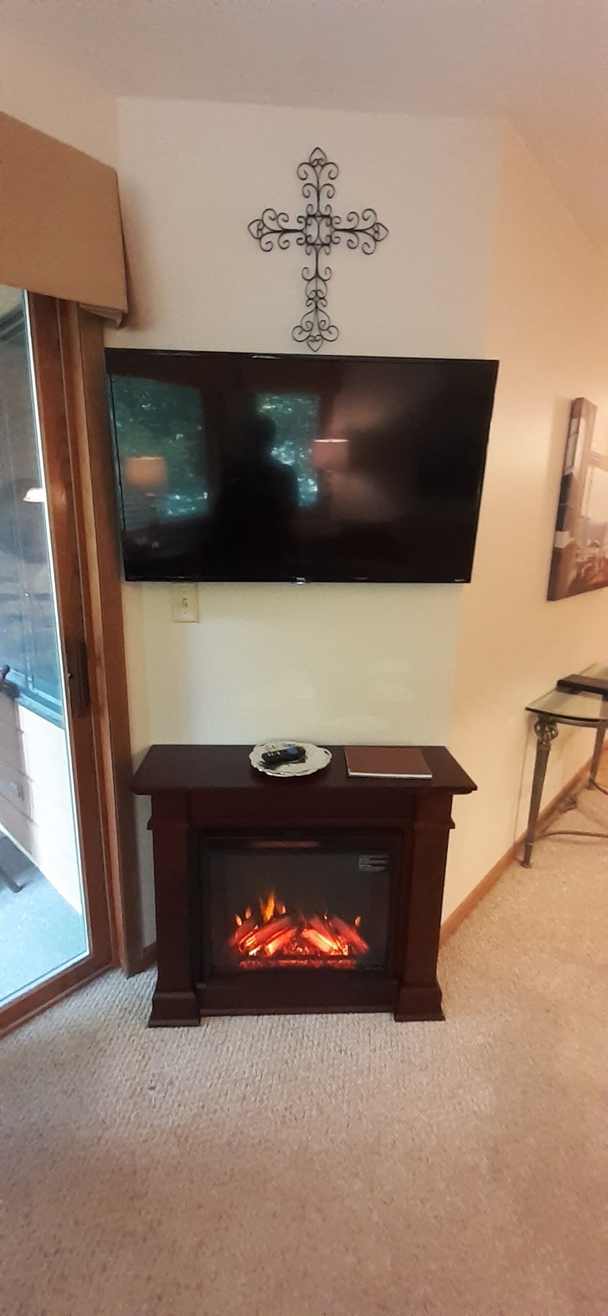 Un salón con un televisor de pantalla plana montado en la pared, una chimenea encendida y una mesita con un control remoto.