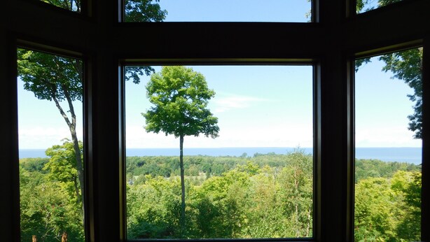 A room with large windows offering a view of a forest and the ocean.