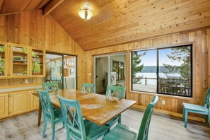 Una cabaña de madera con comedor, ventanas amplias y vista al lago.