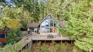 Une cabane dotée d’une grande façade vitrée, d’une terrasse et entourée d’arbres.