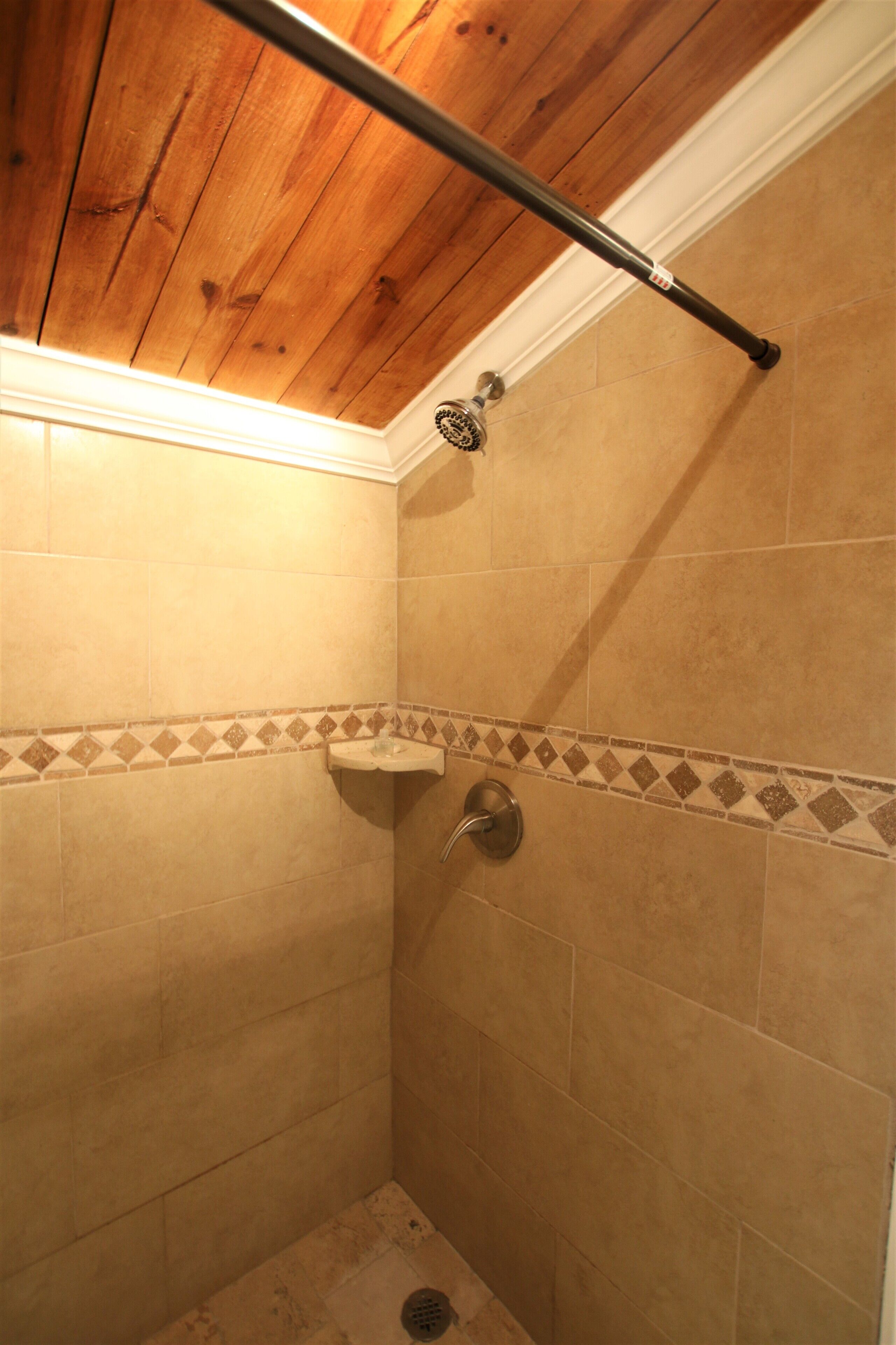 Ducha con azulejos color beige, techo de madera y una barra de metal.