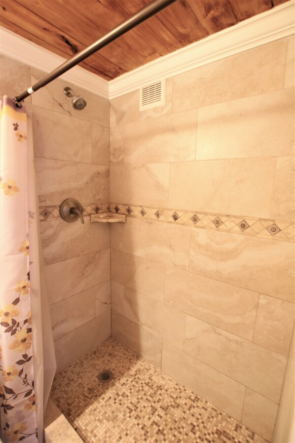 A shower with a tiled wall, a showerhead, and a drain.