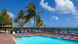 A pool area with blue chairs and a view of the ocean.