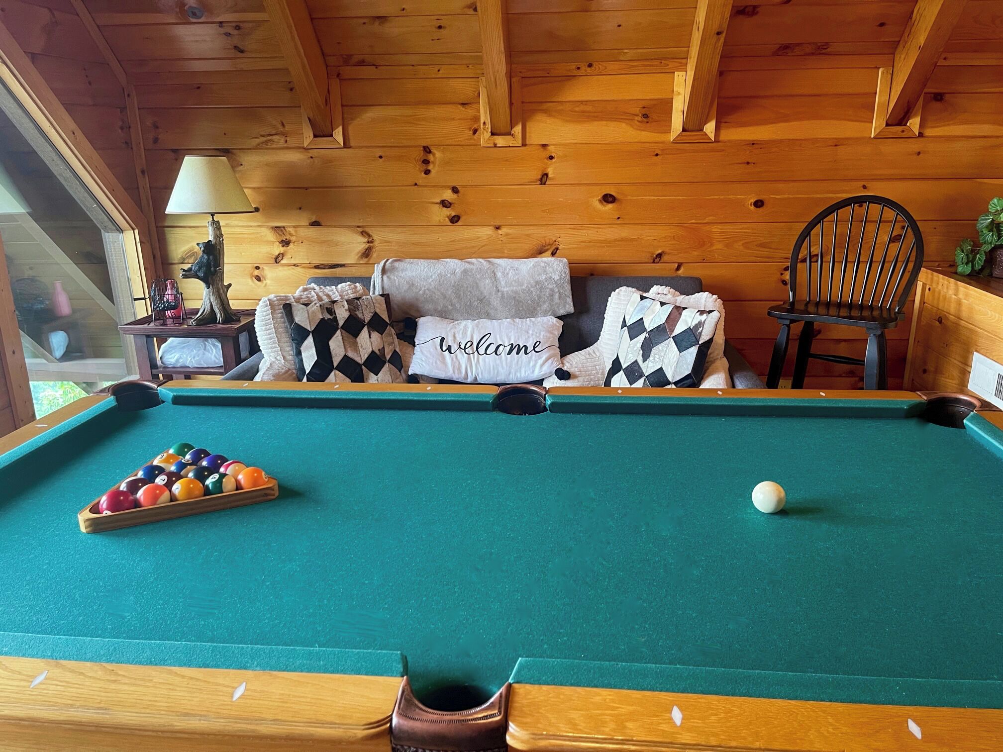 Een pooltafel met een 'welcome' kussen, een stoel en een lamp in een houten kamer.