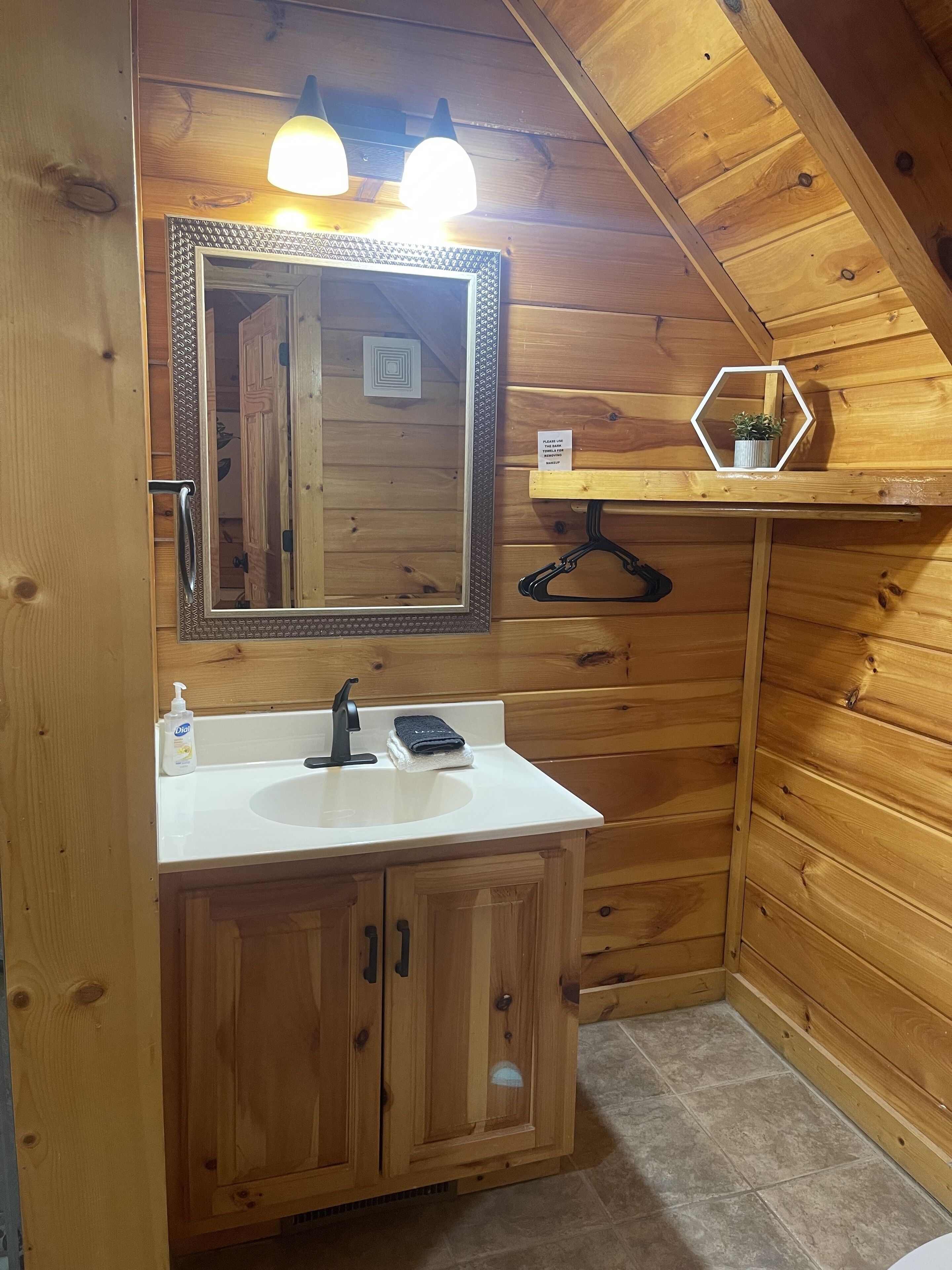 Baño de cabaña de madera con lavamanos, espejo y dos lámparas colgantes.