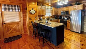 A wooden cabin kitchen with a central island, bar stools, a clock, and modern appliances.