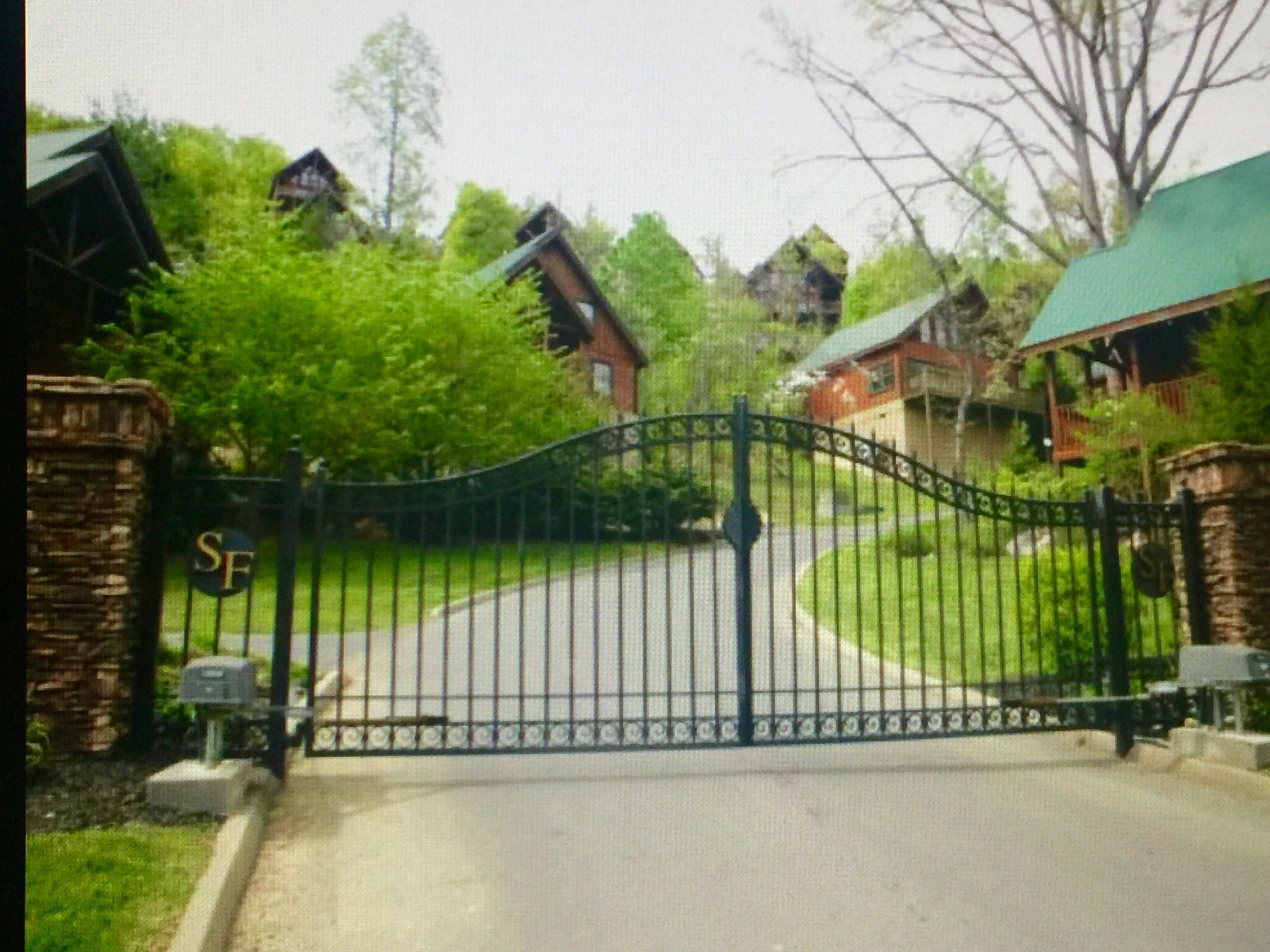 A gated driveway leading to a row of houses with a stone wall on one side.