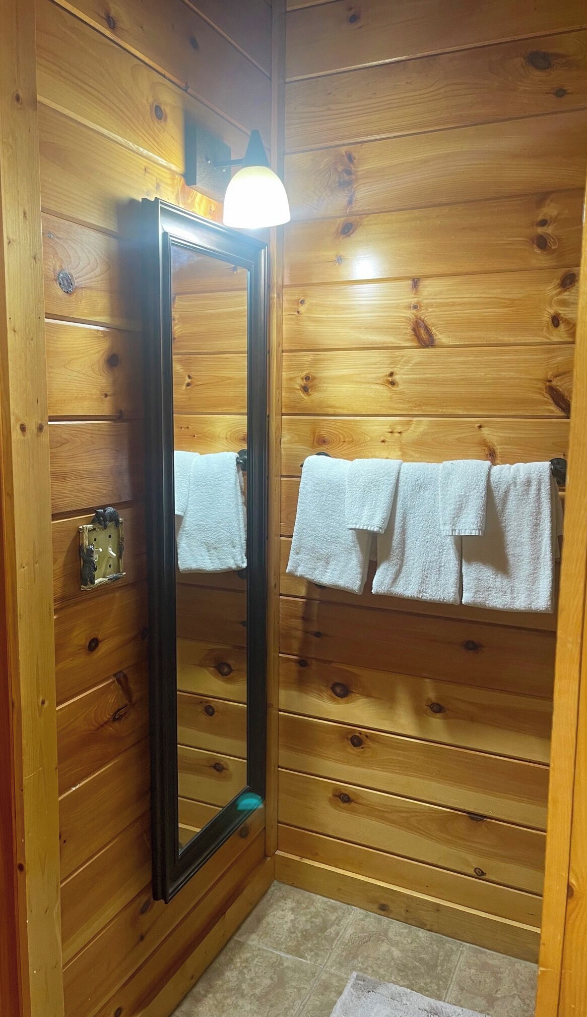 Baño de cabaña de madera con espejo, dos toallas blancas y una lámpara.