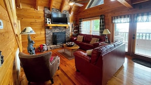 A cozy cabin interior with a stone fireplace, leather sofa, and a television mounted above it.