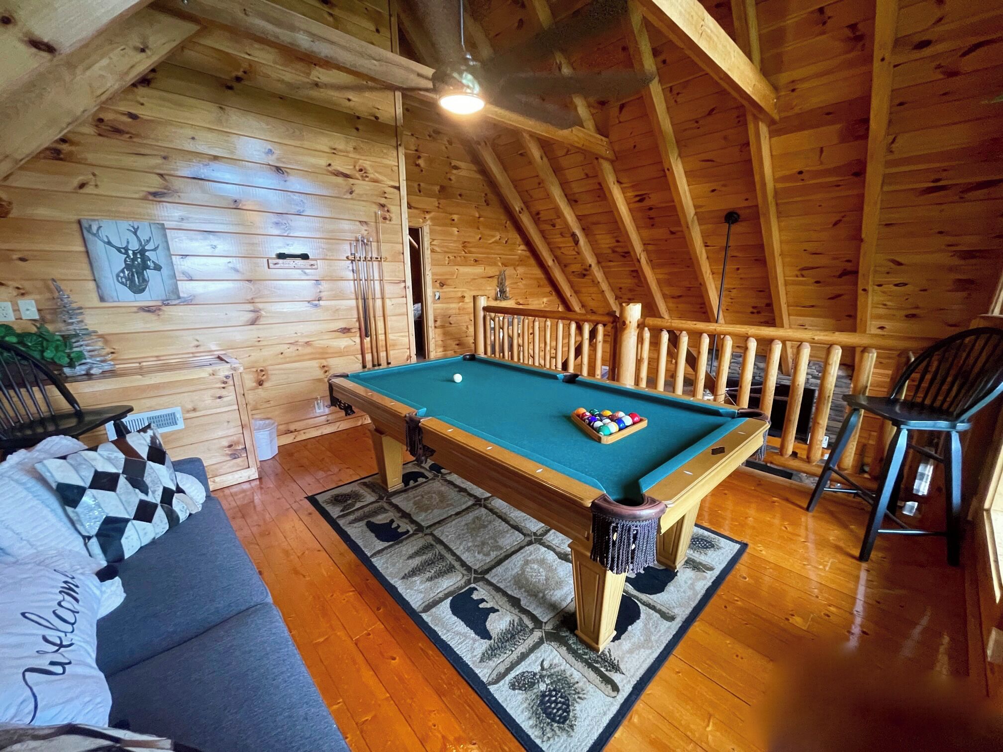 A wooden interior with a pool table, a sofa, and a chair.