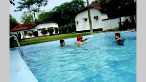 Una piscina con agua cristalina, rodeada por un edificio blanco con techo rojo y abundante vegetación.