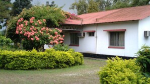 Un edificio blanco con techo rojo, rodeado de setos cuidados y un árbol en flor.