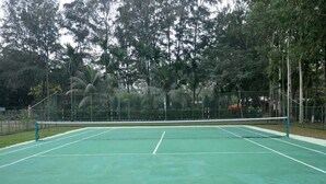 Una cancha de tenis al aire libre con red, rodeada de árboles y una valla.