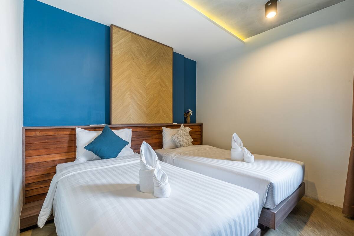 A hotel room with two beds, wooden headboards, and a blue accent wall.
