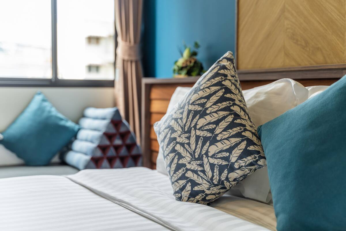 A neatly made bed with patterned pillows and a view of a cityscape through a window.