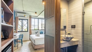 Een moderne hotelkamer met een bed, een zithoek, een badkamer met een groot wastafelmeubel en spiegel, en uitzicht op de stad door grote ramen.