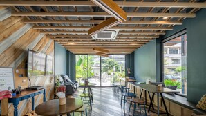 Een modern café met houten balken in het plafond, grote ramen en diverse zitmogelijkheden, waaronder tafels en stoelen.