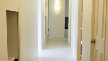 A narrow, well-lit hallway with a light fixture at the end, leading to a room with a ceiling vent and a door on the right.