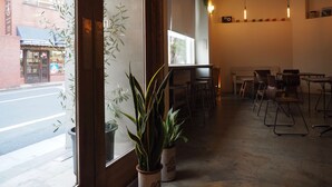 A cafe interior with a large window, potted plants, and a seating area with tables and chairs. - almond hostel & cafe Shibuya (Tokyo)