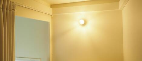Una habitación con una cama, una ventana con cortinas y una lámpara fijada a la pared.