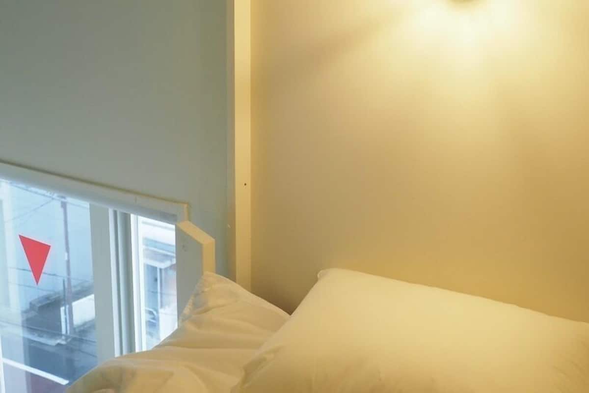 A room with a bed, a window with a red triangular sign, and a light fixture on the wall.
