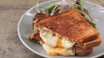 Sándwich de queso a la plancha con queso derretido y una ensalada al lado en un plato.
