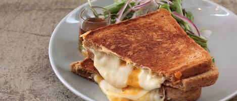 A grilled cheese sandwich with melted cheese and a side salad on a plate.