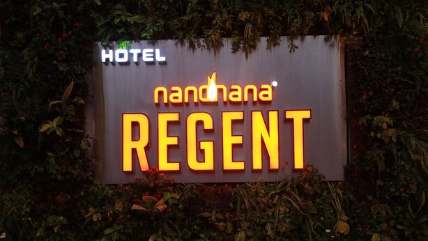 Een hotelschild met de naam 'nanohana REGENT' verlicht in felgele letters voor een donkere achtergrond.