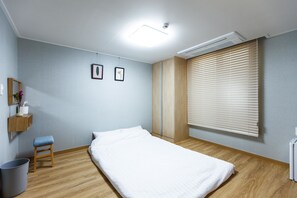 A bedroom with a bed, a small stool, a wall-mounted shelf with a vase, and a window with blinds. - Sunrise Dadam (Seogwipo)